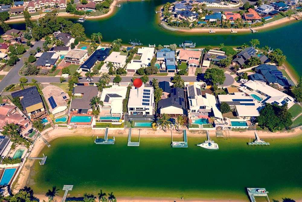 Aerial view of luxury houses on the waterways of the Gold Coast with a red pin on one of the houses